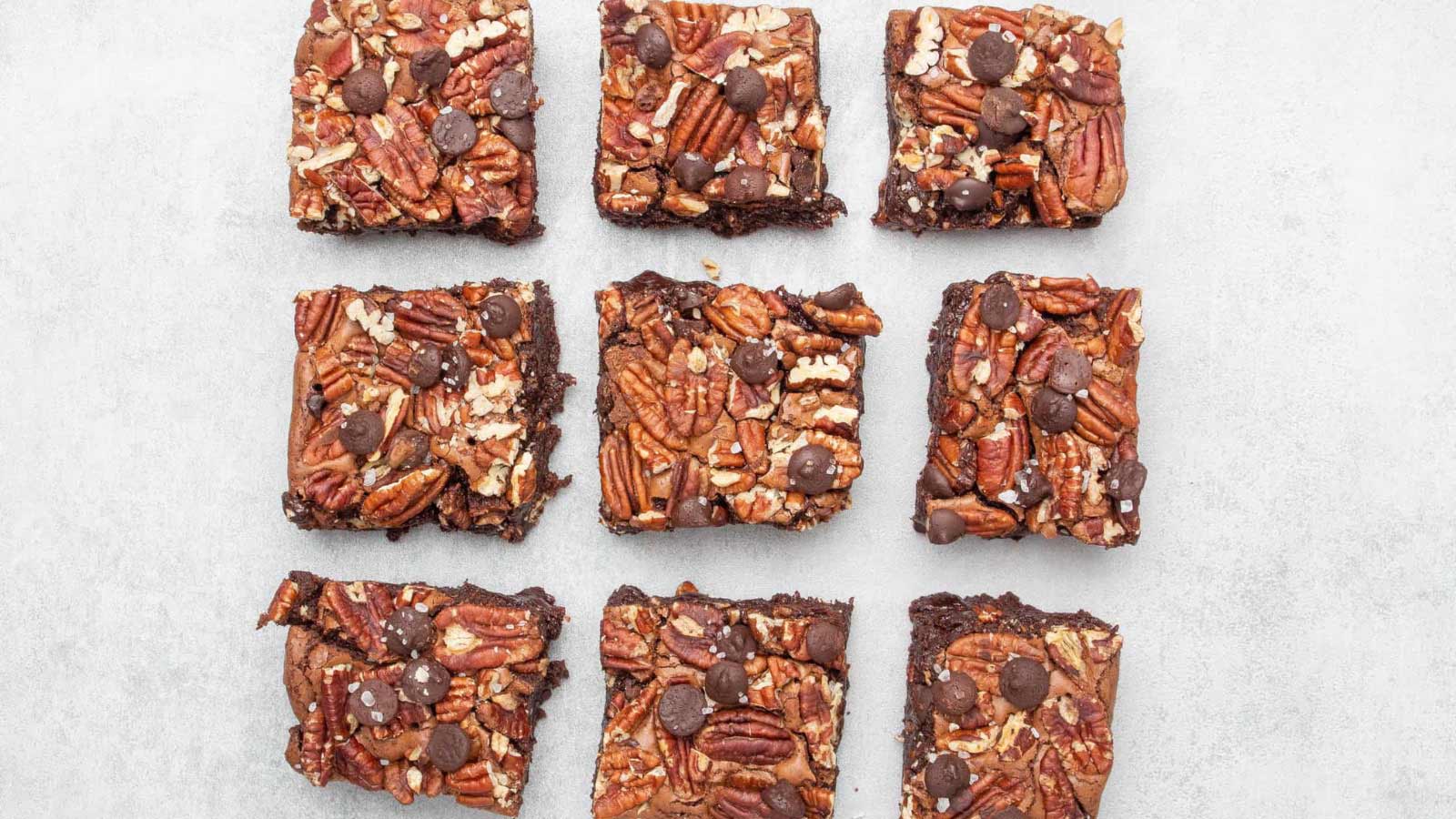 An overhead view of fudge pecan brownies cut and lined up in rows on white parchment.