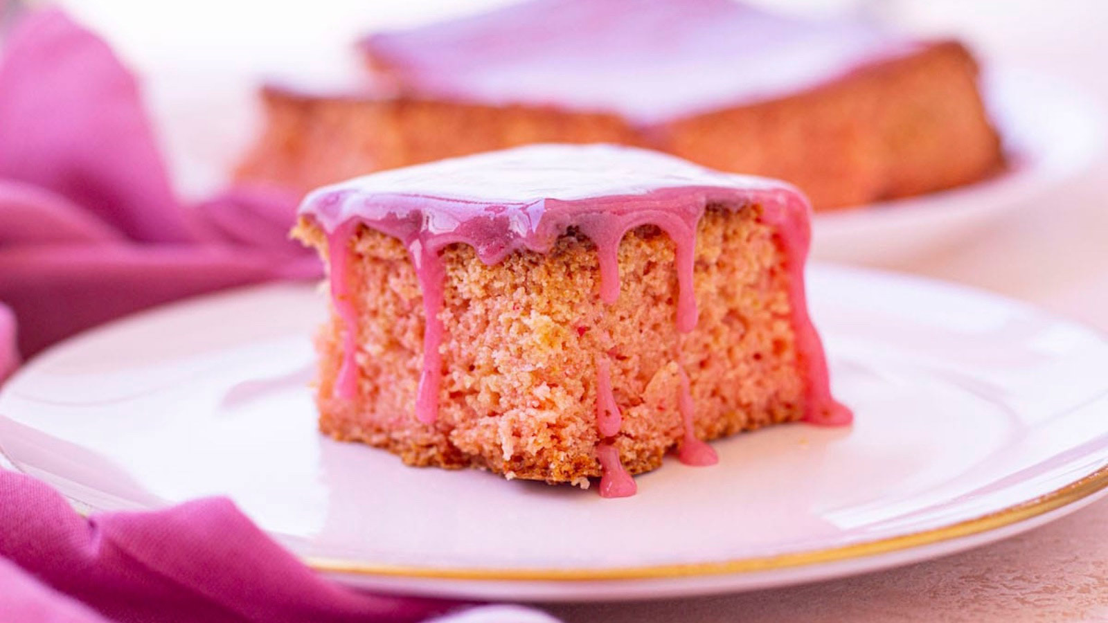 A single strawberry brownie with frosting dripping down the edges on a white plate.