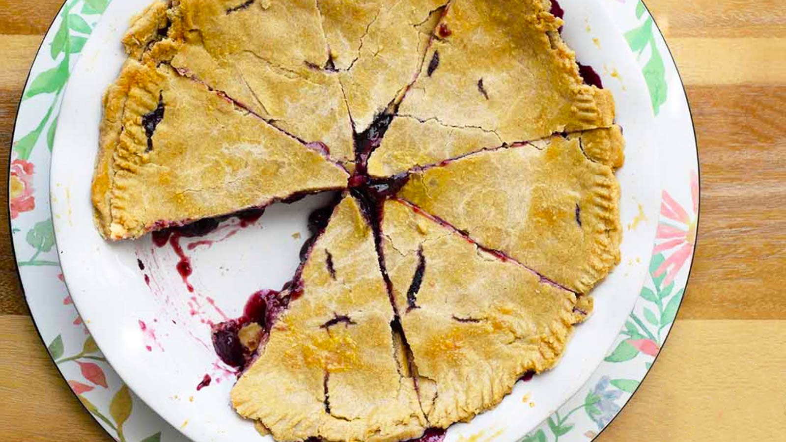 An overhead view of a whole blueberry pie, sliced with one slice missing.