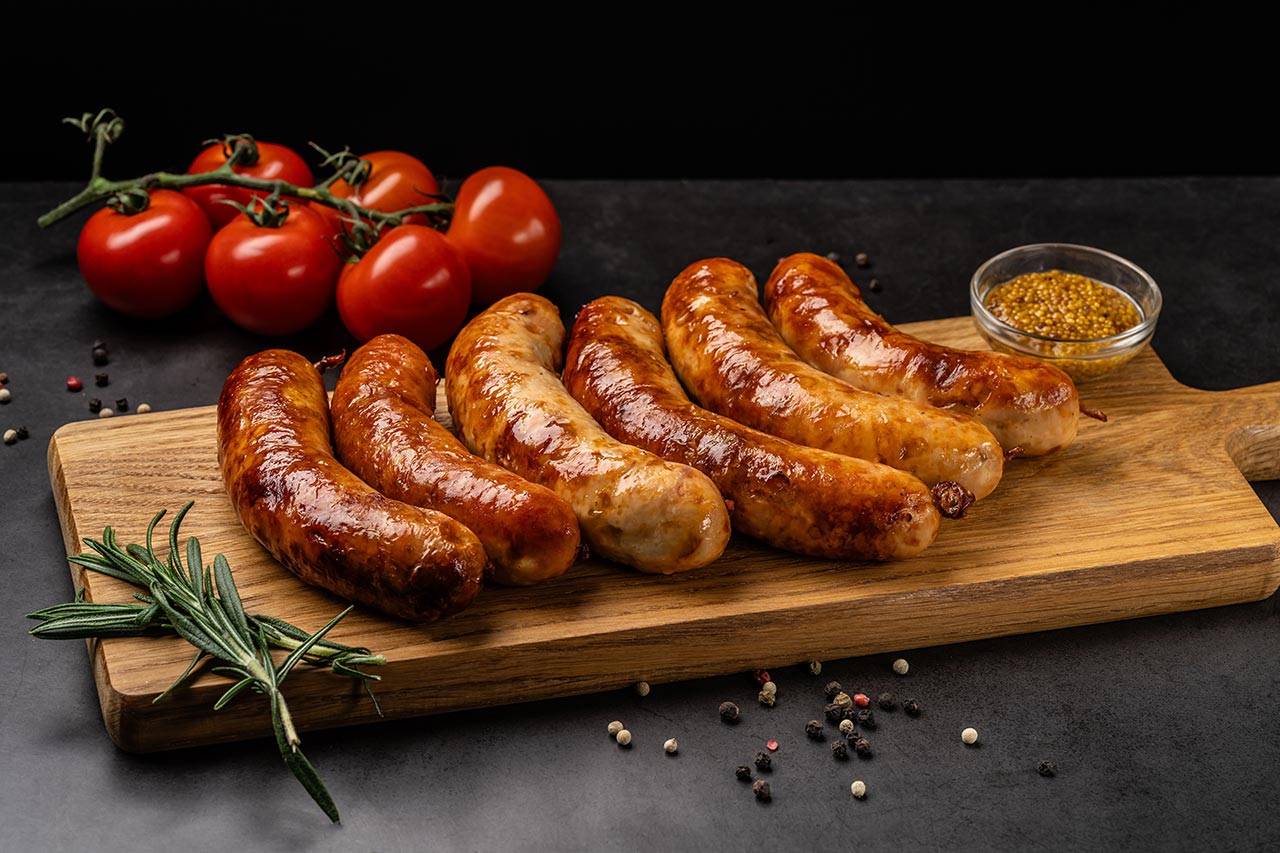 German cuisine. Juicy fried bratwurst sausages lie on a wooden board, on a black background.