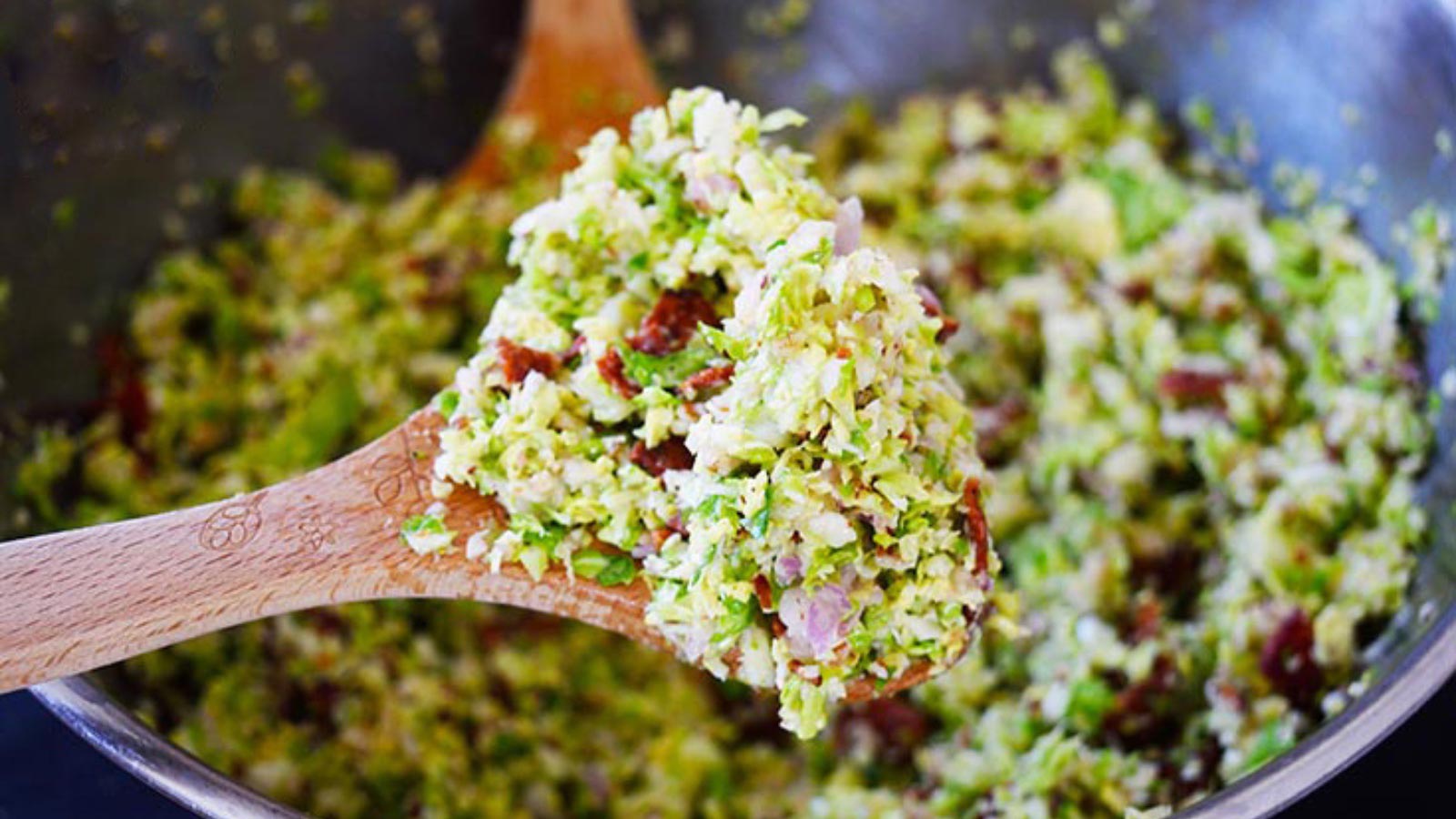 A wooden spoon holds up a spoonful of Brussels Sprouts Salad.