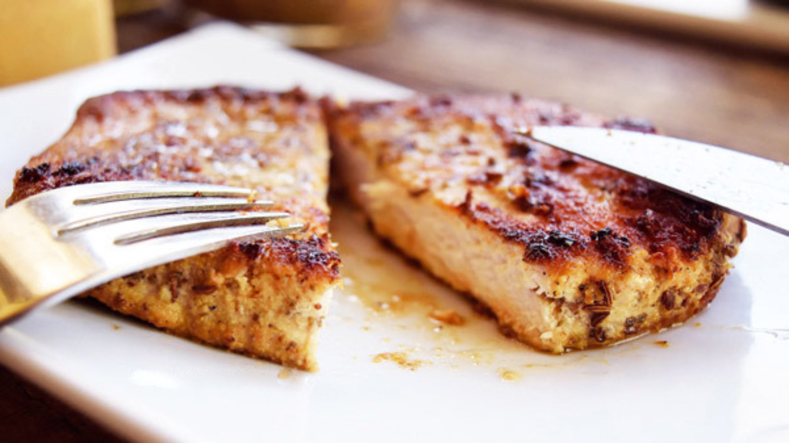A pork chop on a white plat with a knife and fork, cut in half.