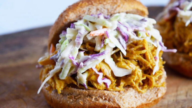 A closeup of a Carolina Gold BBQ Chicken sandwich topped with creamy coleslaw on a whole grain bun.