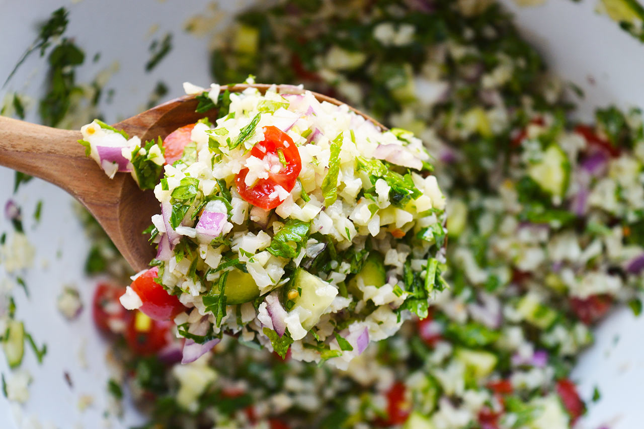 A closeup of a wooden spoon full of Cauliflower Tabouleh.