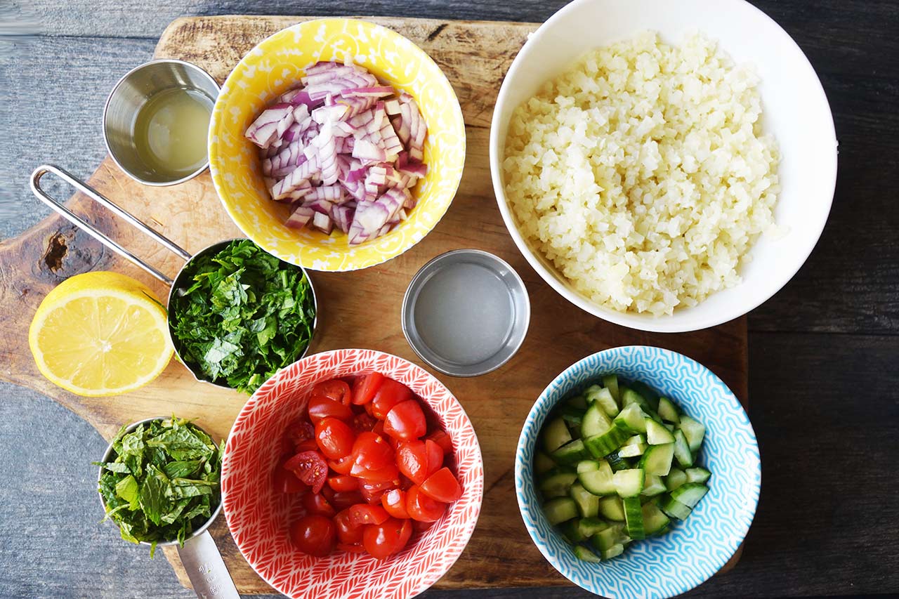 Cauliflower Tabouleh Recipe ingredients measured and in individual bowls on a cutting board.