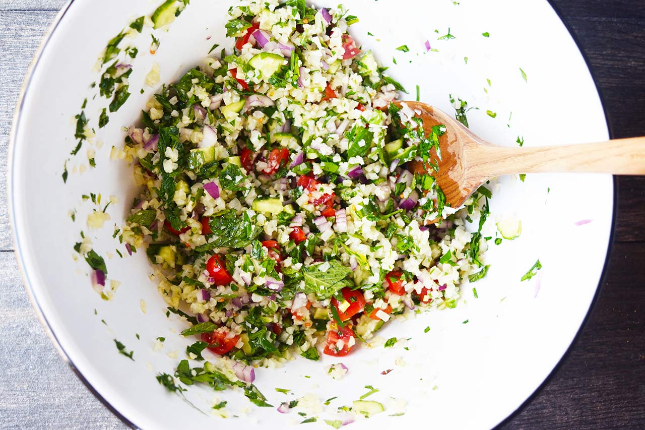 An overhead view of a white bowl with Cauliflower Tabouleh and a wooden spoon.