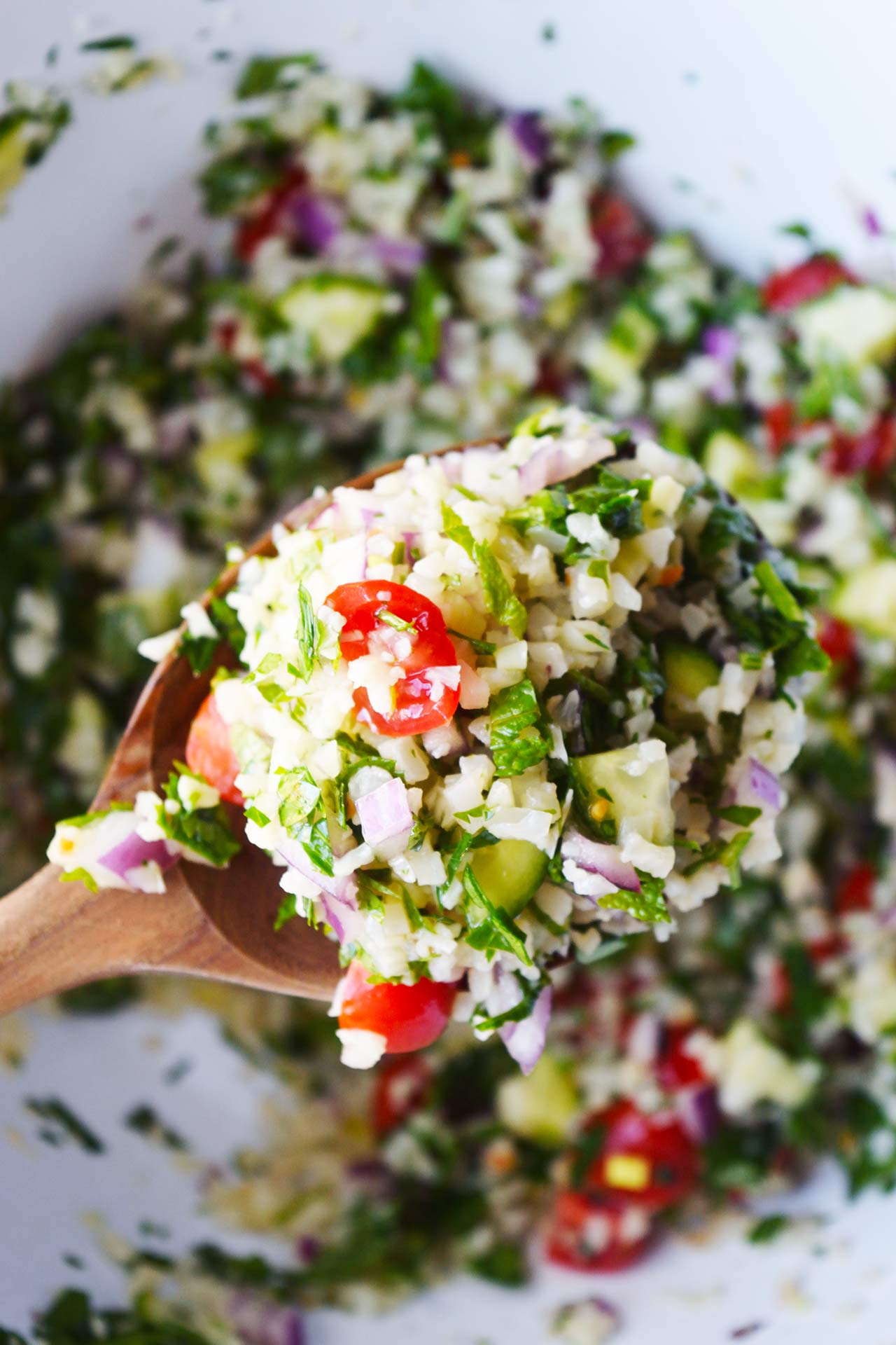 A wooden spoon lifts Cauliflower Tabbouleh out of a mixing bowl.
