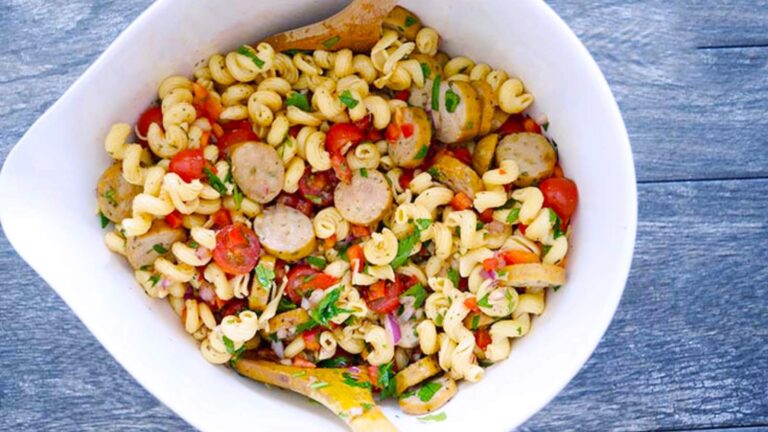 An overhead view of a white mixing bowl filled with cavatappi pasta salad.
