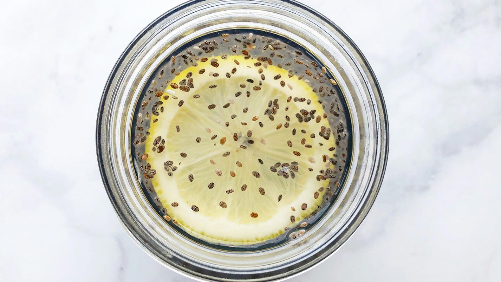 An overhead view of a glass jar filled with chia Fresca with a lemon slice floating in the jar.