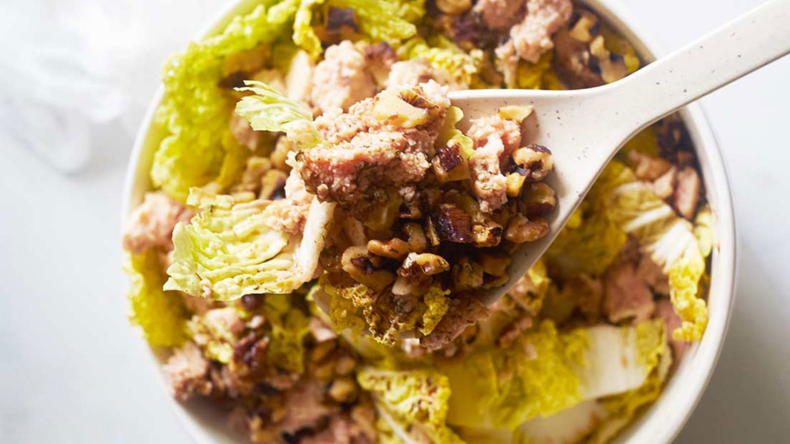 An overhead view of a salad tong lifting some Chicken Endive Salad out of a bowl.