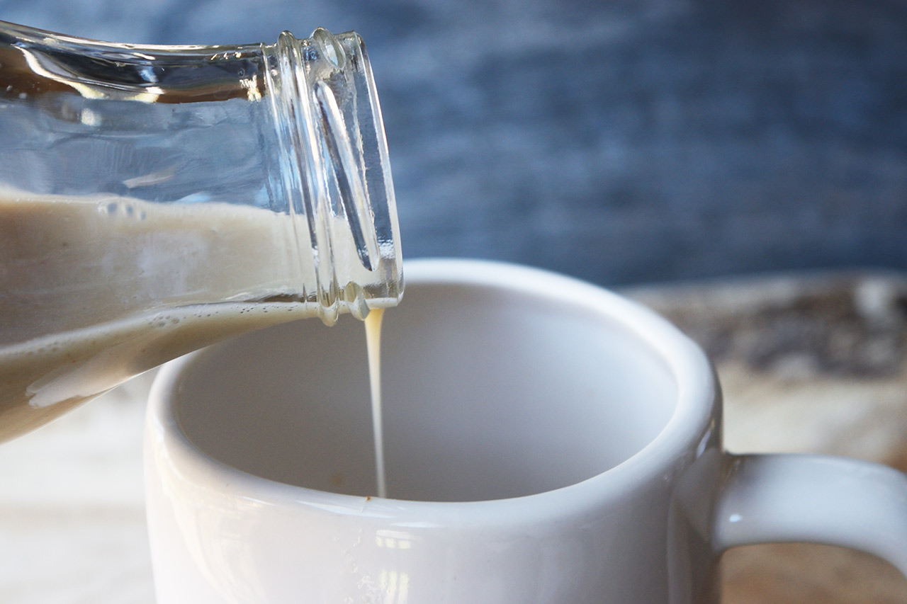 A glass jar pouring some Condensed Milk into a mug.