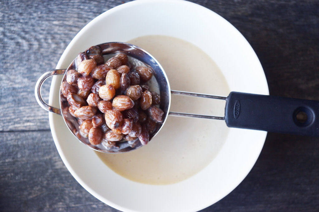 A sieve resting over a bowl filled with soaked raisins.