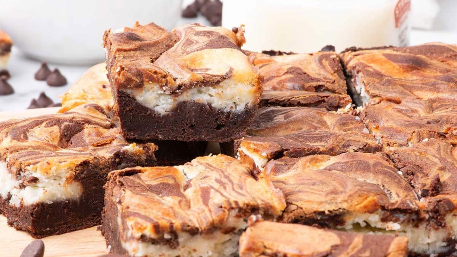 A batch of cut cream cheese brownies on a cutting board. One brownie sits on top of the others.
