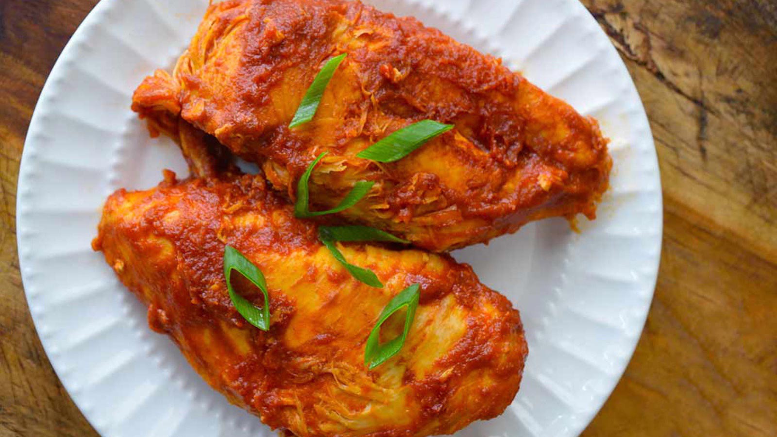 Two BBQ chicken breasts on a white plate, topped with sliced green onions.