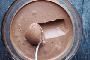 A spoon being scooped over the surface of chocolate mousse into a swirl of mouse on the spoon.