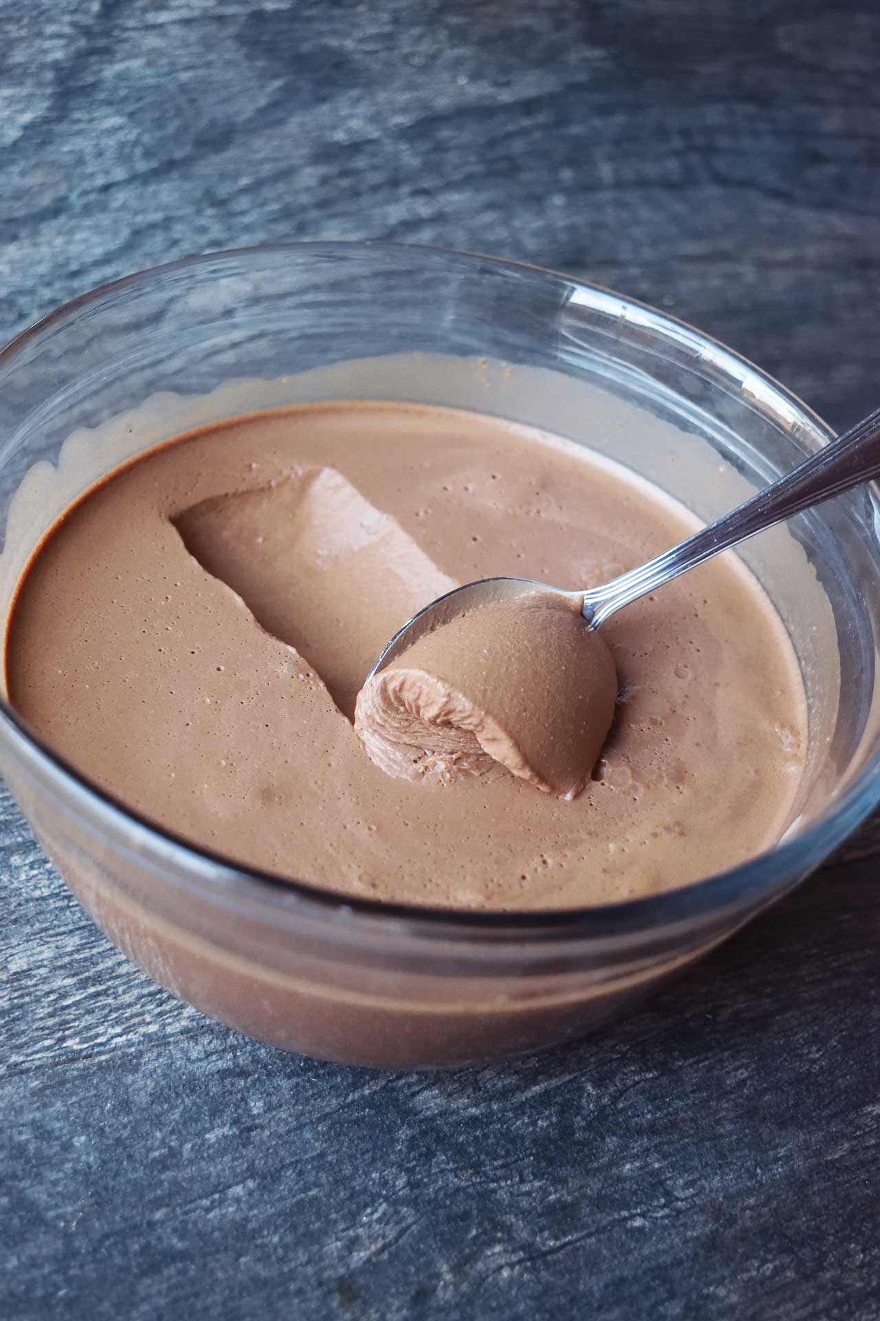 A side view of spoon scooping up chocolate mousse out of a glass bowl.