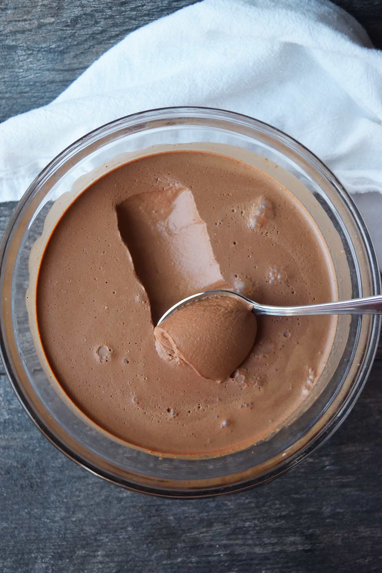 An overhead view of a spoon scooping up chocolate mousse from a bowl.