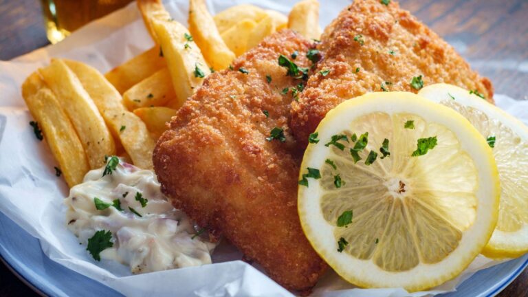 Fish n' chips with lemon slices in a parchment-lined basket.