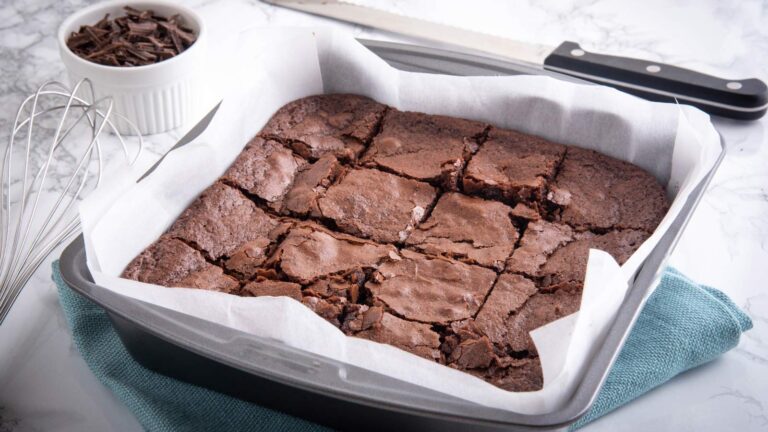 A metal cake pan lined with parchment and filled with baked and cut brownies.
