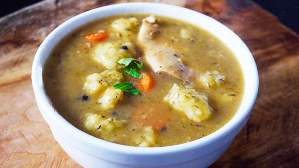 A white bowl sits on a wood surface and is filled with Germany potato dumpling soup.