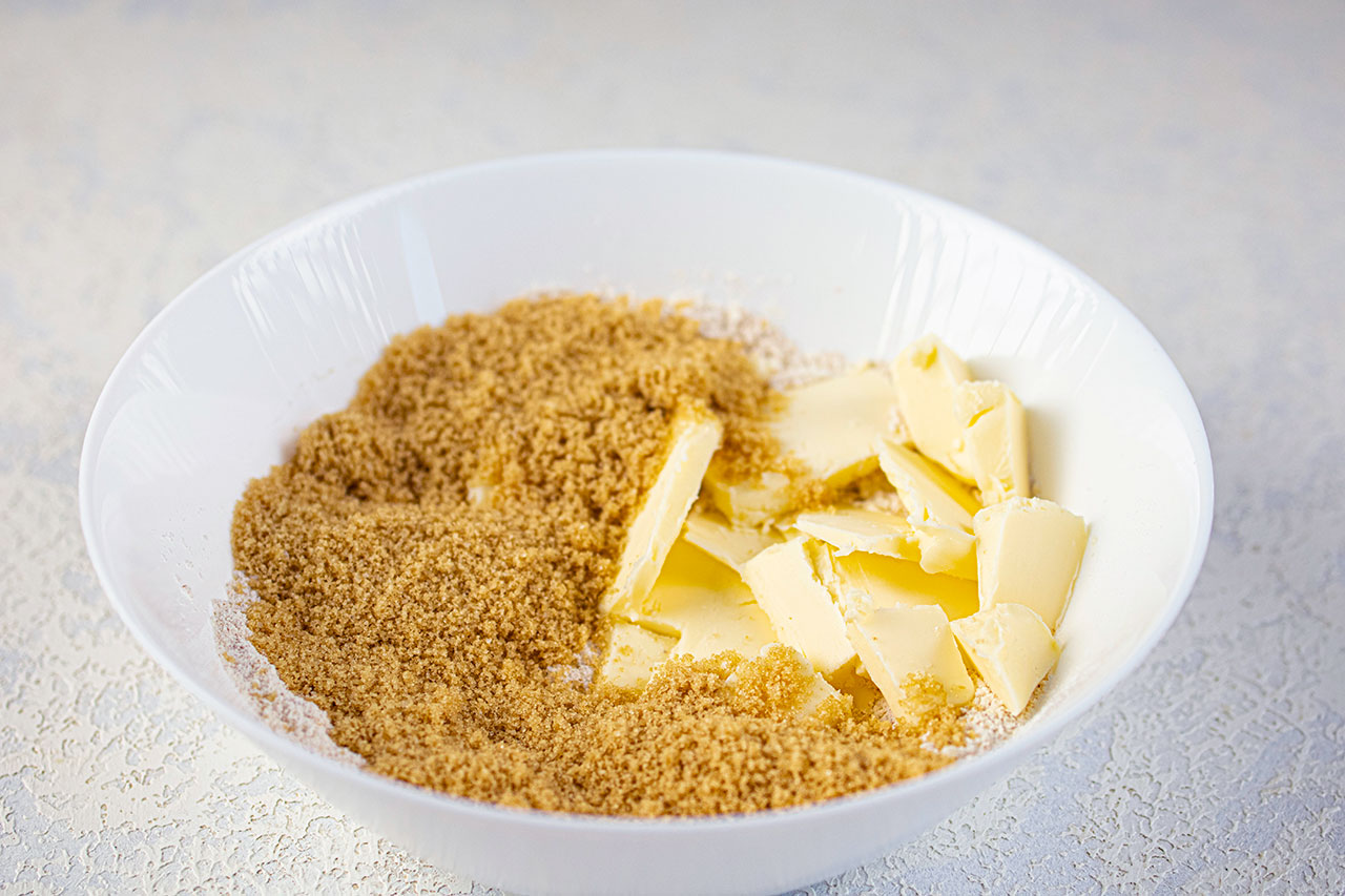A white mixing bowl holds flour, sweetener and cubes of butter.