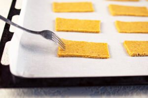 Cut graham crackers on a parchment-lined cookie sheet. A fork pokes holes in the crackers.