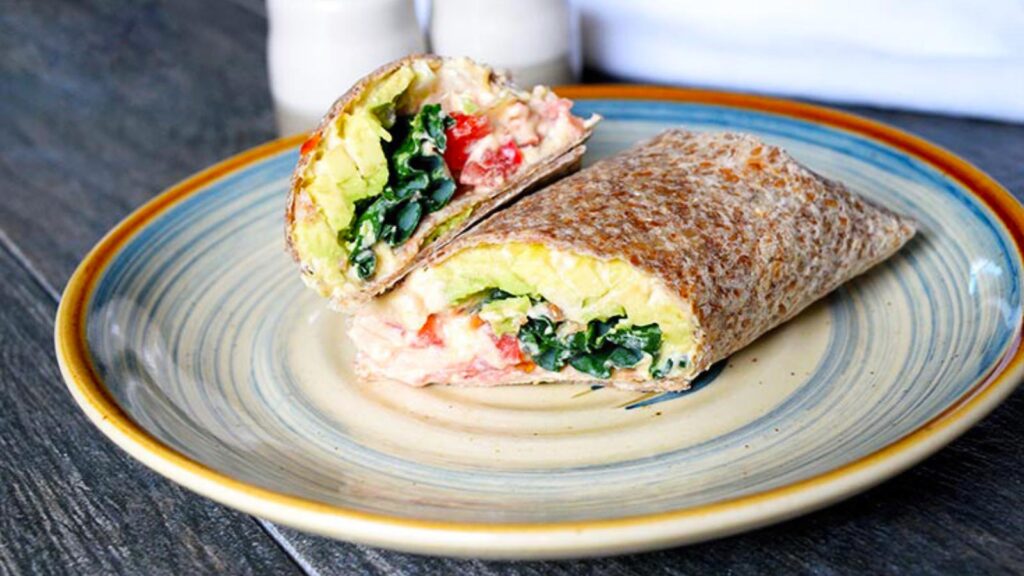 The finished, cut hummus wrap on a plate, ready to eat.