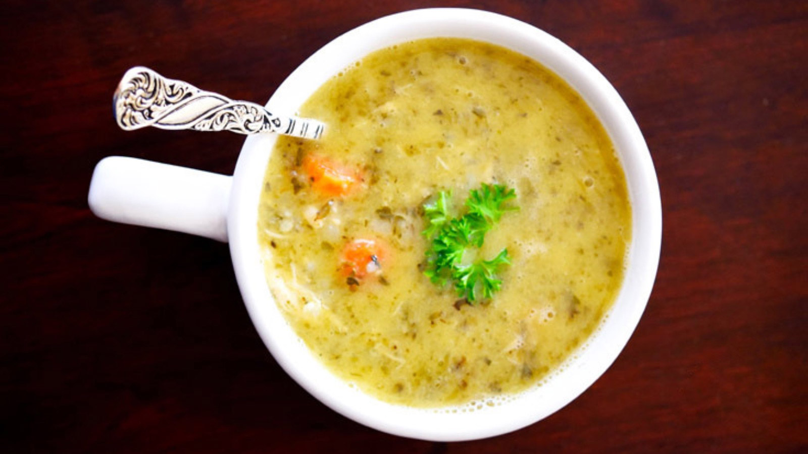 An overhead view of a white mug filled with chickens out. A spoon sits in the soup.