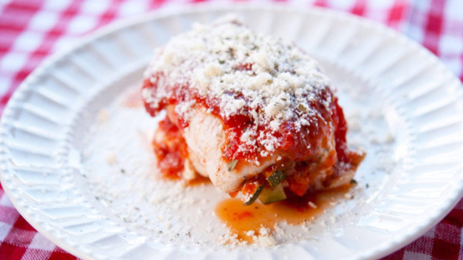 A single Italian Stuffed Chicken Breast on a white plate topped with grated parmesan cheese.