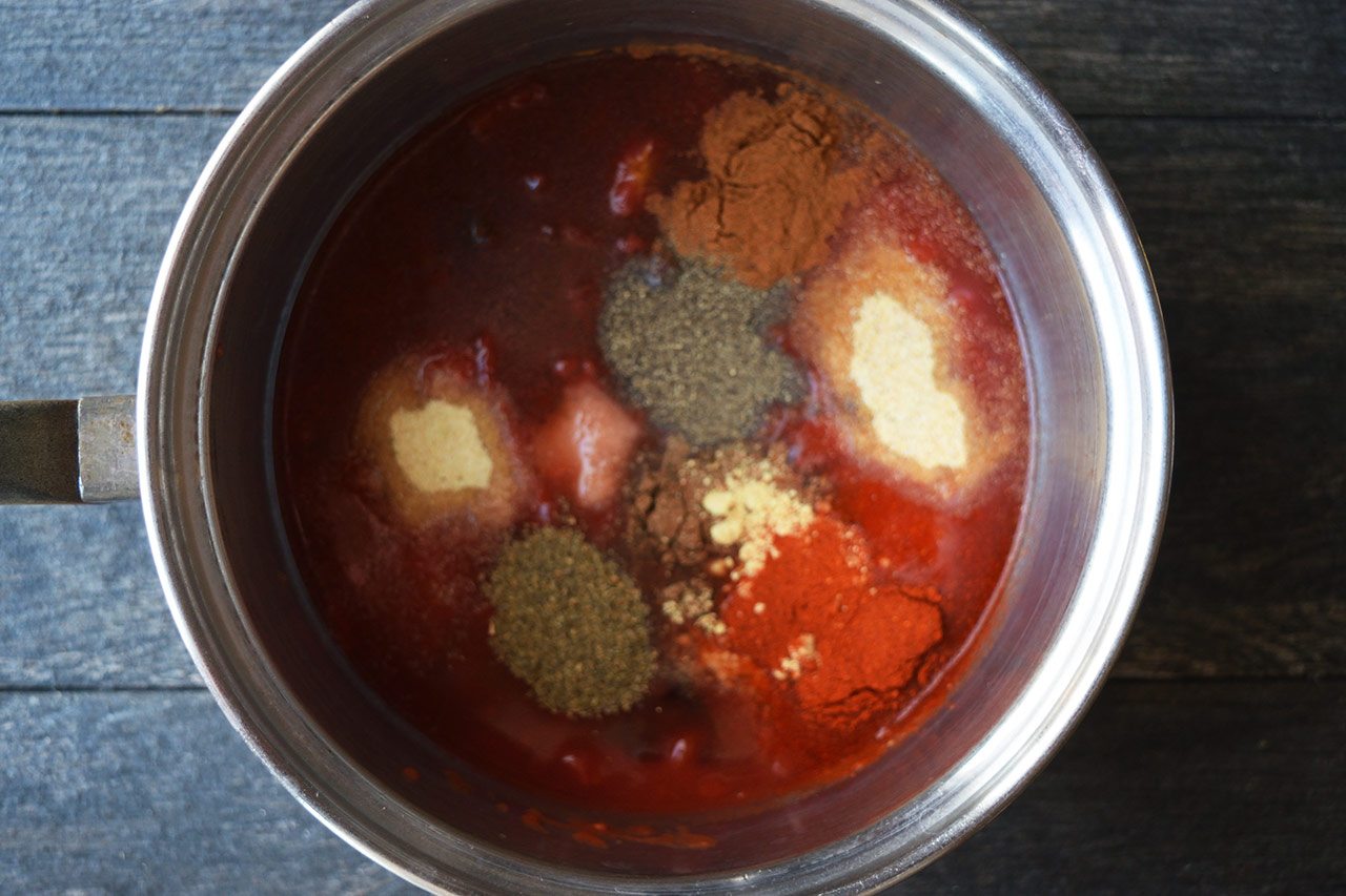 Spices added to tomatoes, vinegar, and maple syrup in a pot.