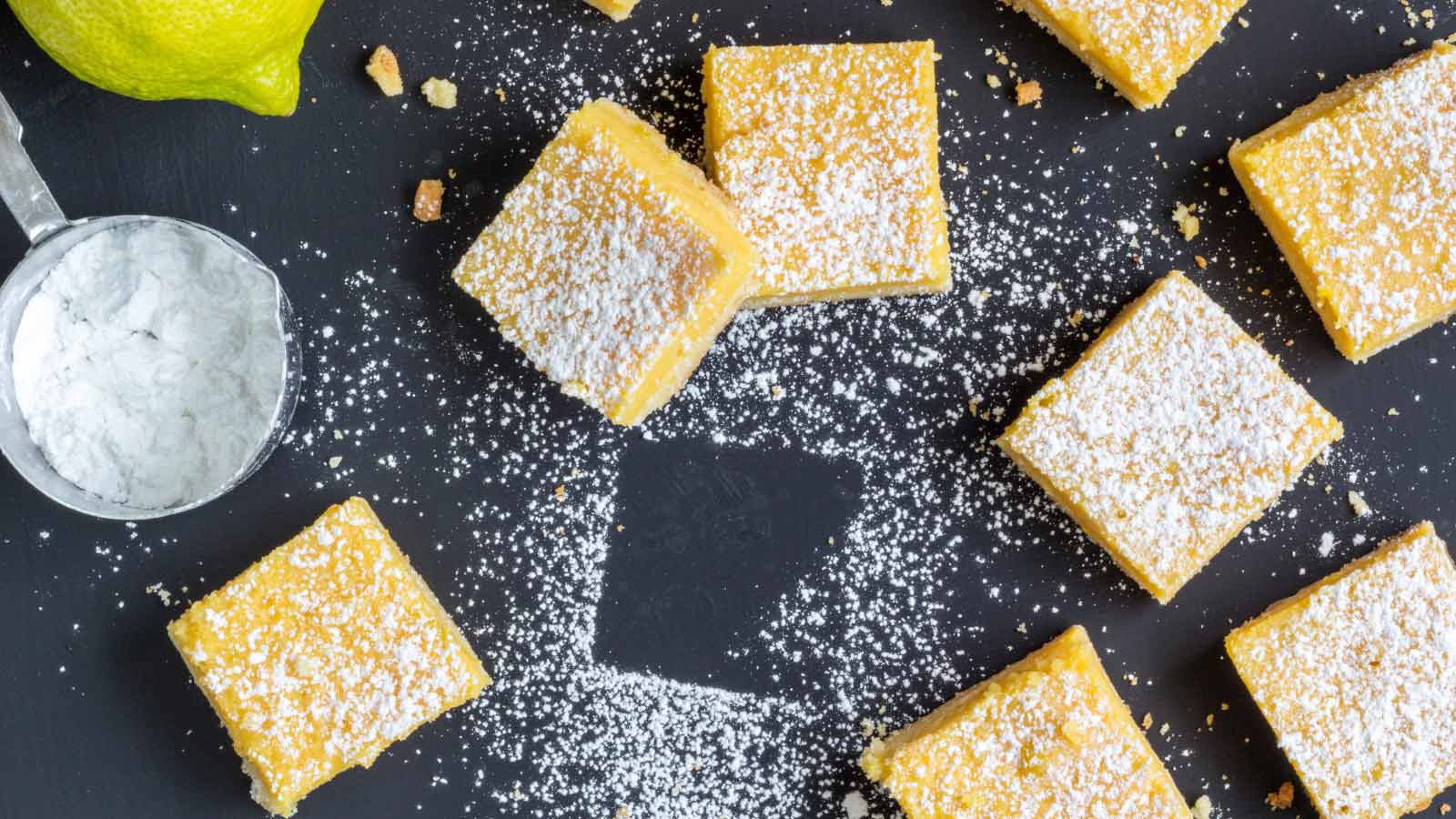 An overhead view of cut lemon bar squares on a black surface.