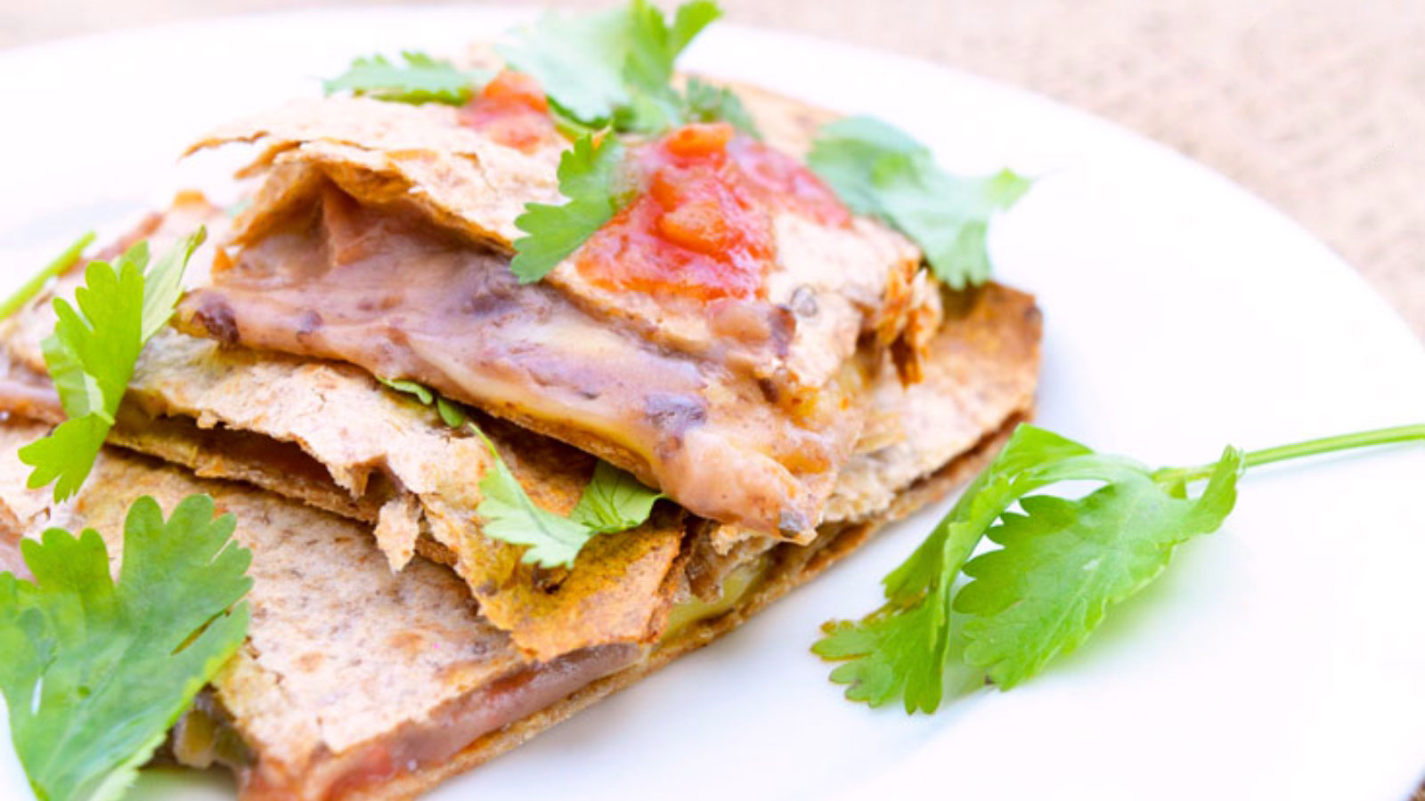 A portion of loaded sheet pan quesadilla sitting on a white plate, garnished with fresh cilantro.