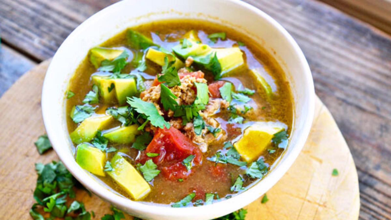 A white bowl filled with Slow Cooker Taco Soup and topped with fresh avocado chunks and fresh herbs.