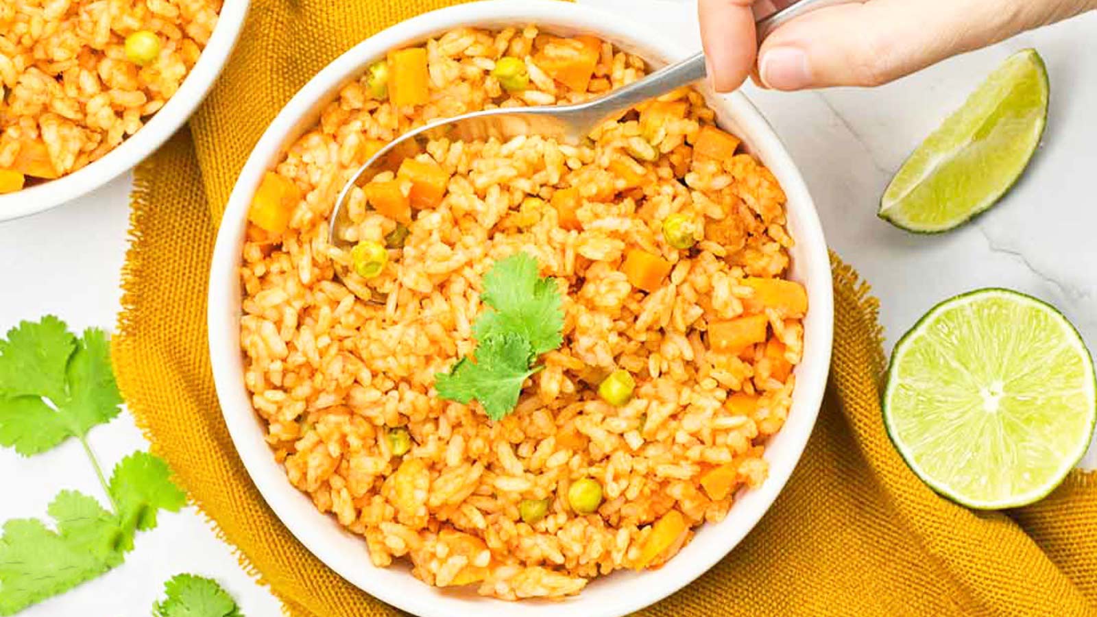 A hand spoons some Mexican rice out of a white bowl full of it.