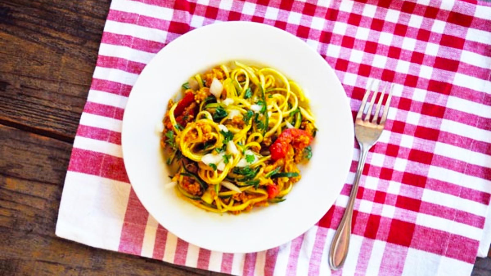 An overhead view of a white bowl filled with Mexican Zpaghetti sitting on a red and white checkered placemat.