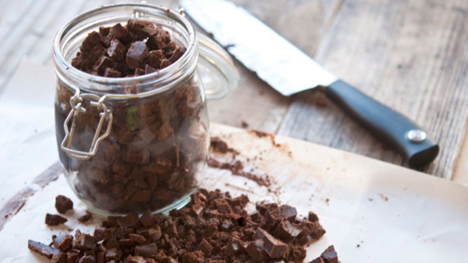Homemade Mint Chocolate Chips in an open glass jar that sits on a cutting board with more chocolate chips.