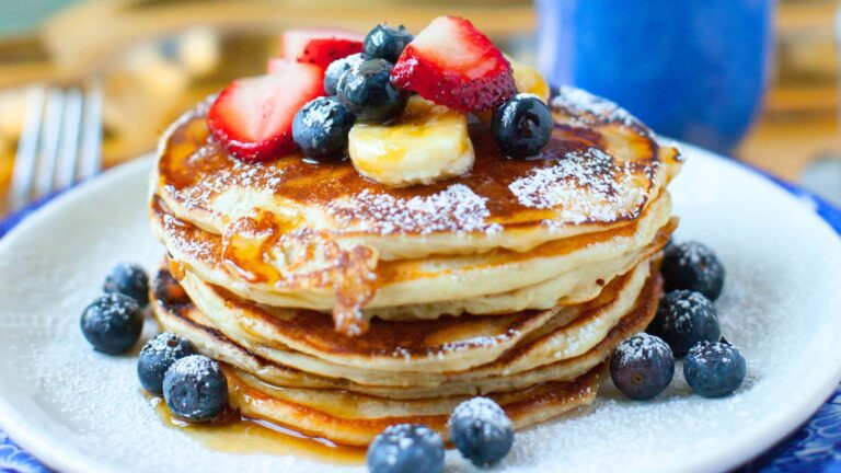 A stack of pancakes with fresh strawberries and blueberries on a white plate.