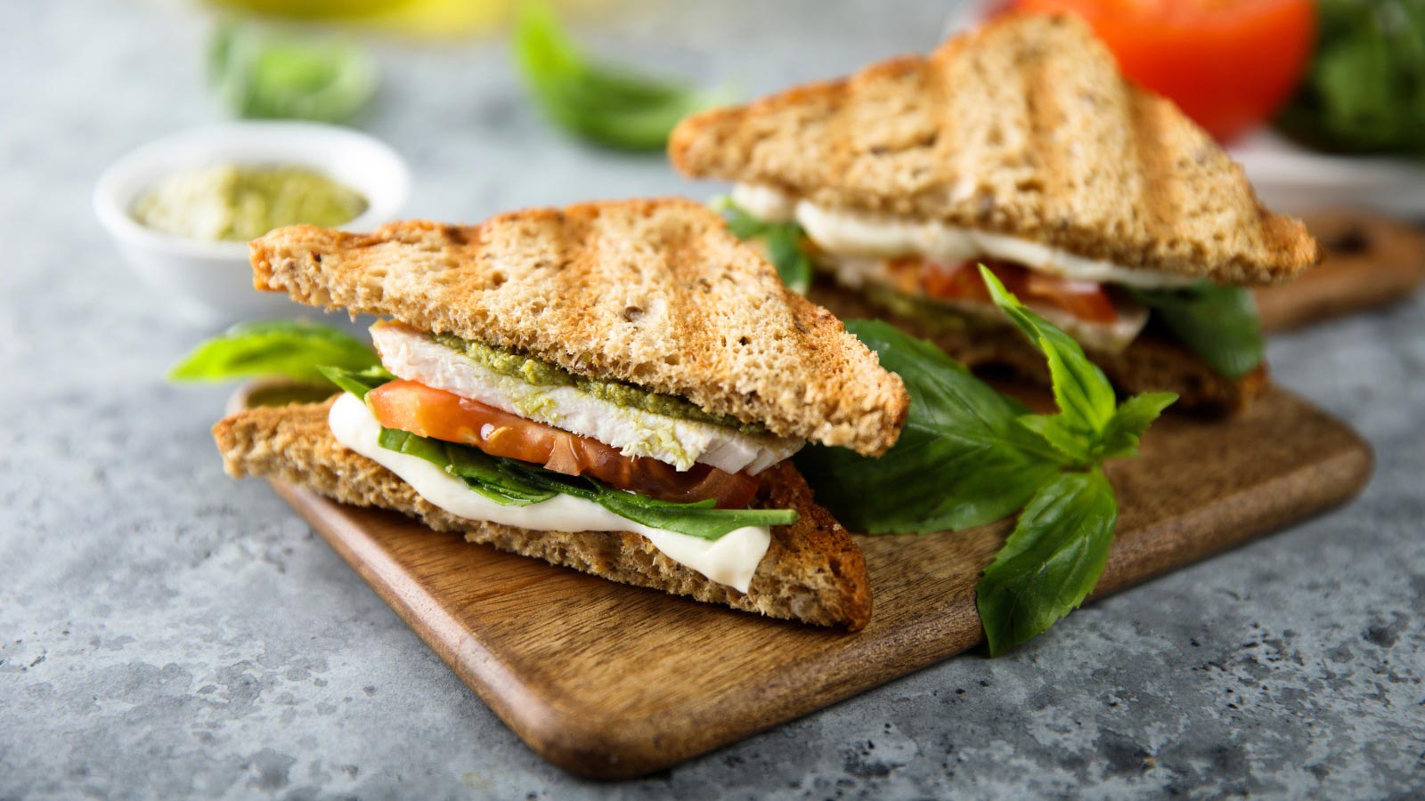 A pesto turkey sandwich cut in half, laying on a cutting board.