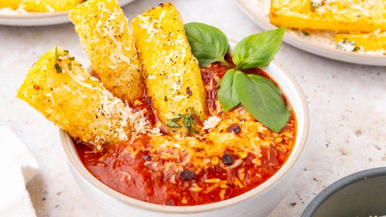 A white bowl with marinara and three polenta fries resting in the sauce.