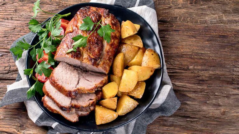 Roast pork with herbs and vegetables on rustic wooden table.