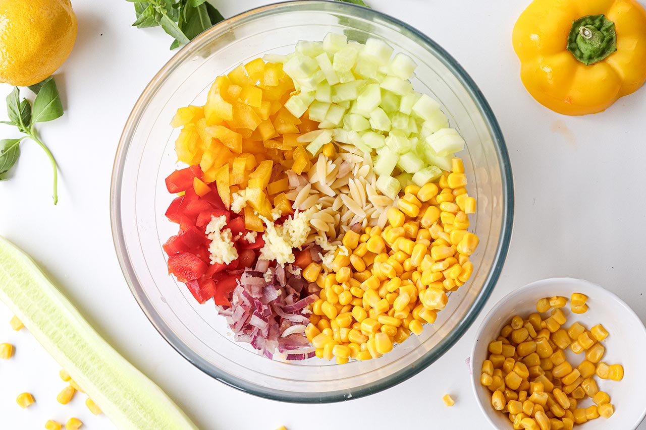 The orzo salad ingredients in a glass mixing bowl, unmixed.