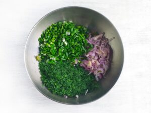 Onions, herbs and chives added to pickles in a mixing bowl.