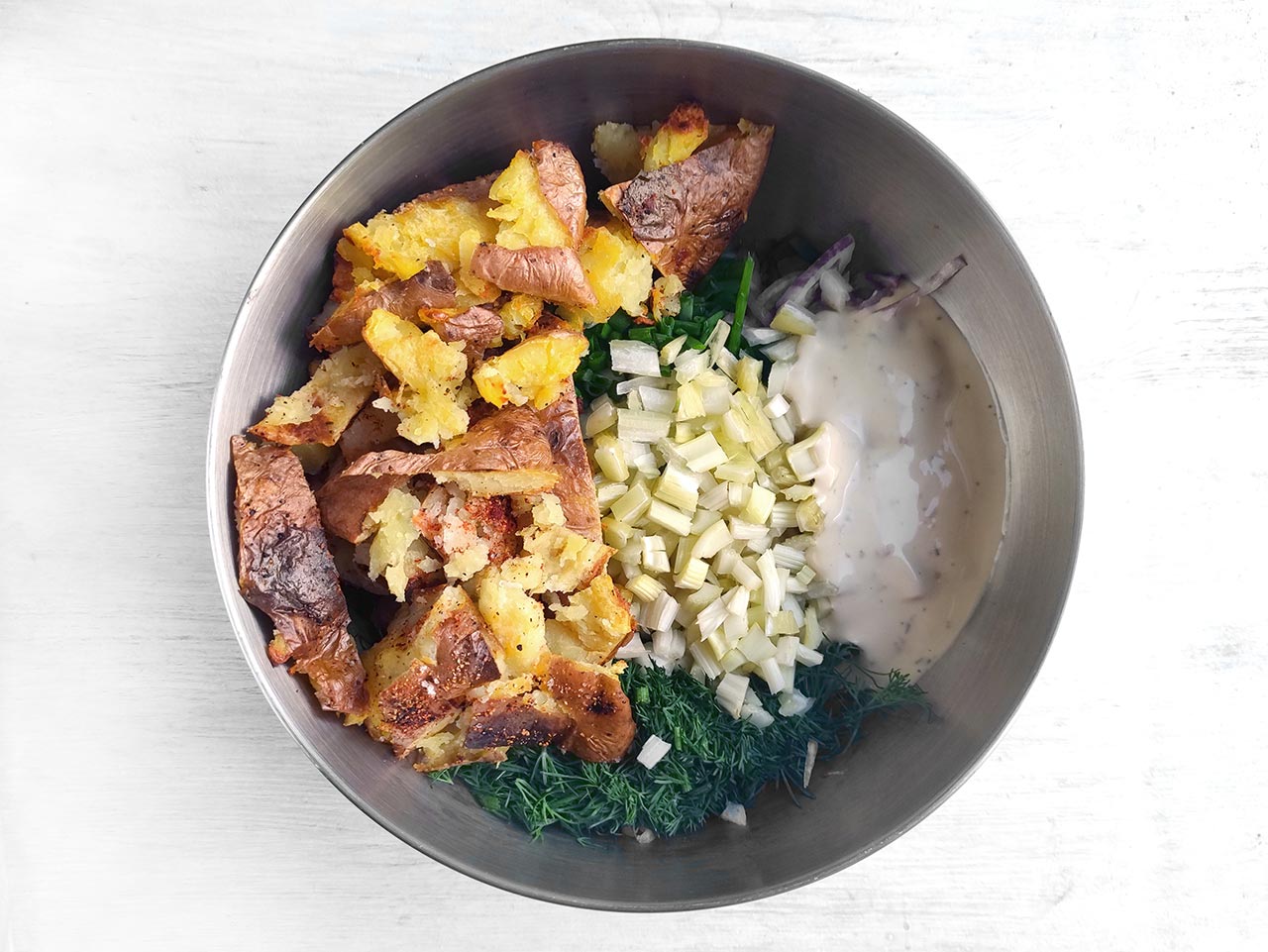 Smashed potatoes added to a mixing bowl with the rest of the recipe ingredients.