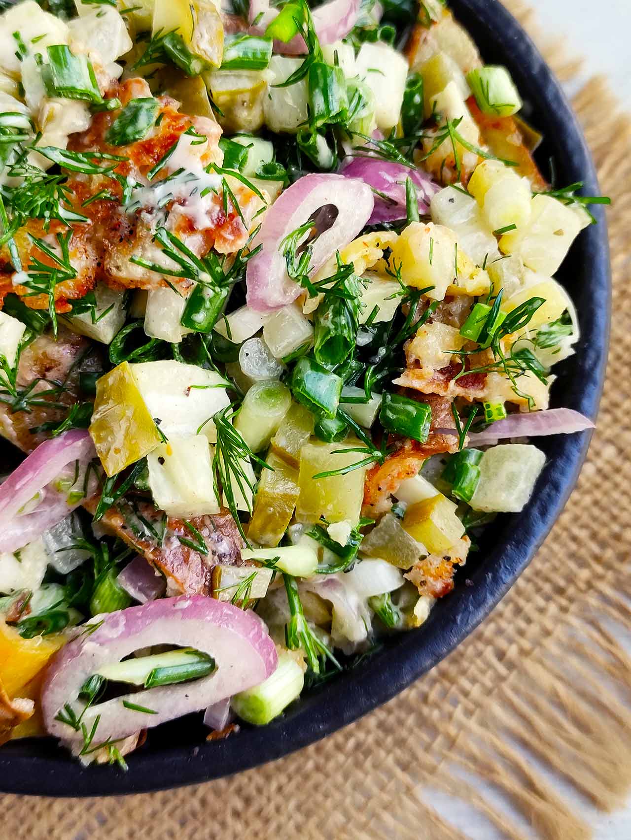 An overhead closeup of a black bowl filled with Red Potato Salad.