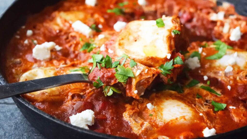 A serving spoon rests in a skillet full of Shakshuka.