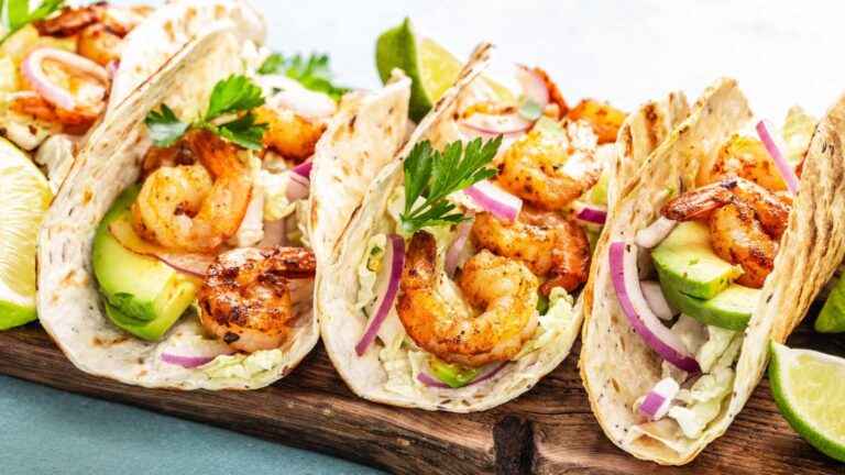 Shrimp tacos in tortillas served on wooden cutting board.