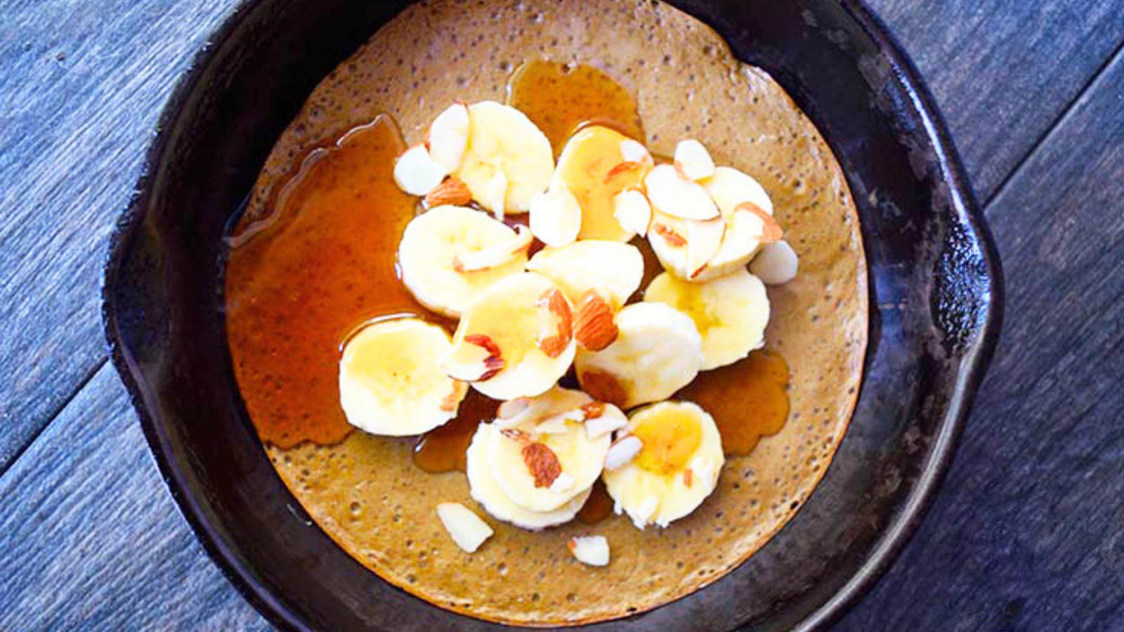 The finished skillet pancake topped with sliced bananas, sliced almonds and maple syrup.