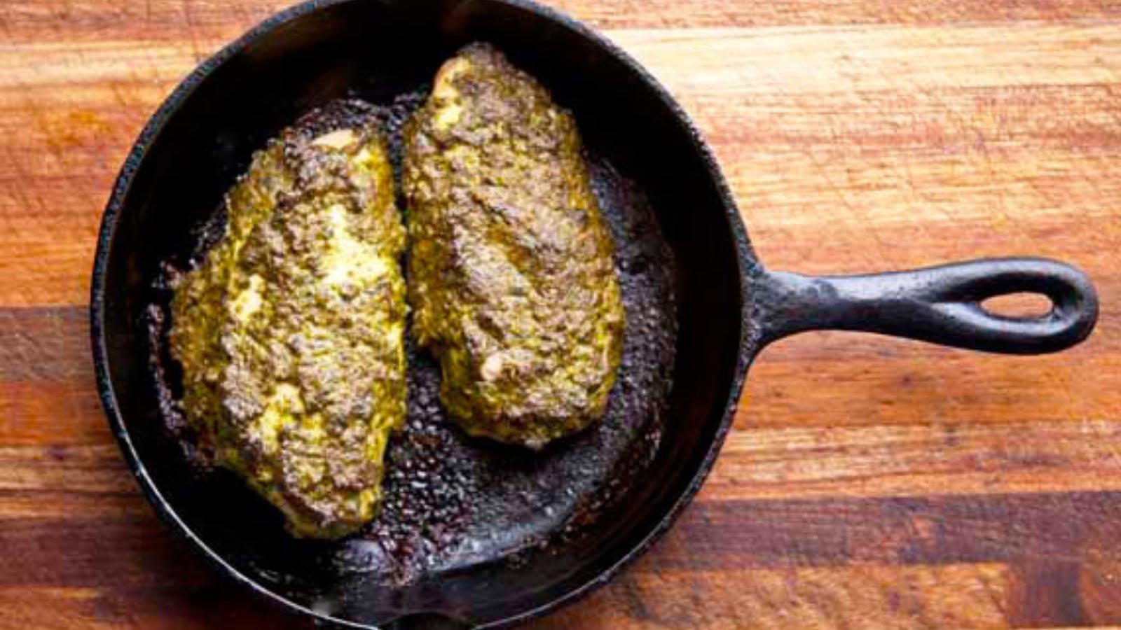 Two baked pesto chicken breasts in a cast iron skillet.