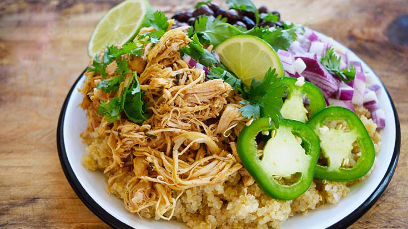 Slow Cooker Cilantro Lime Chicken served over quinoa and garnished with jalapeno pepper slices, lime slices, onions and black beans.