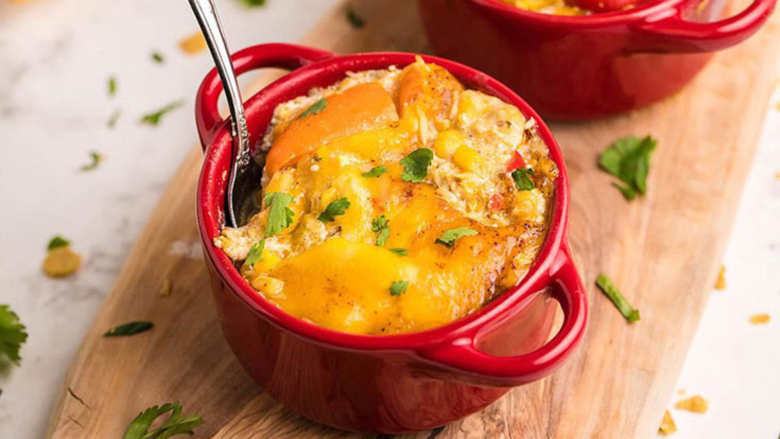Two small, red casserole dishes filled with Super Easy Slow Cooker Chicken Enchilada Casserole.